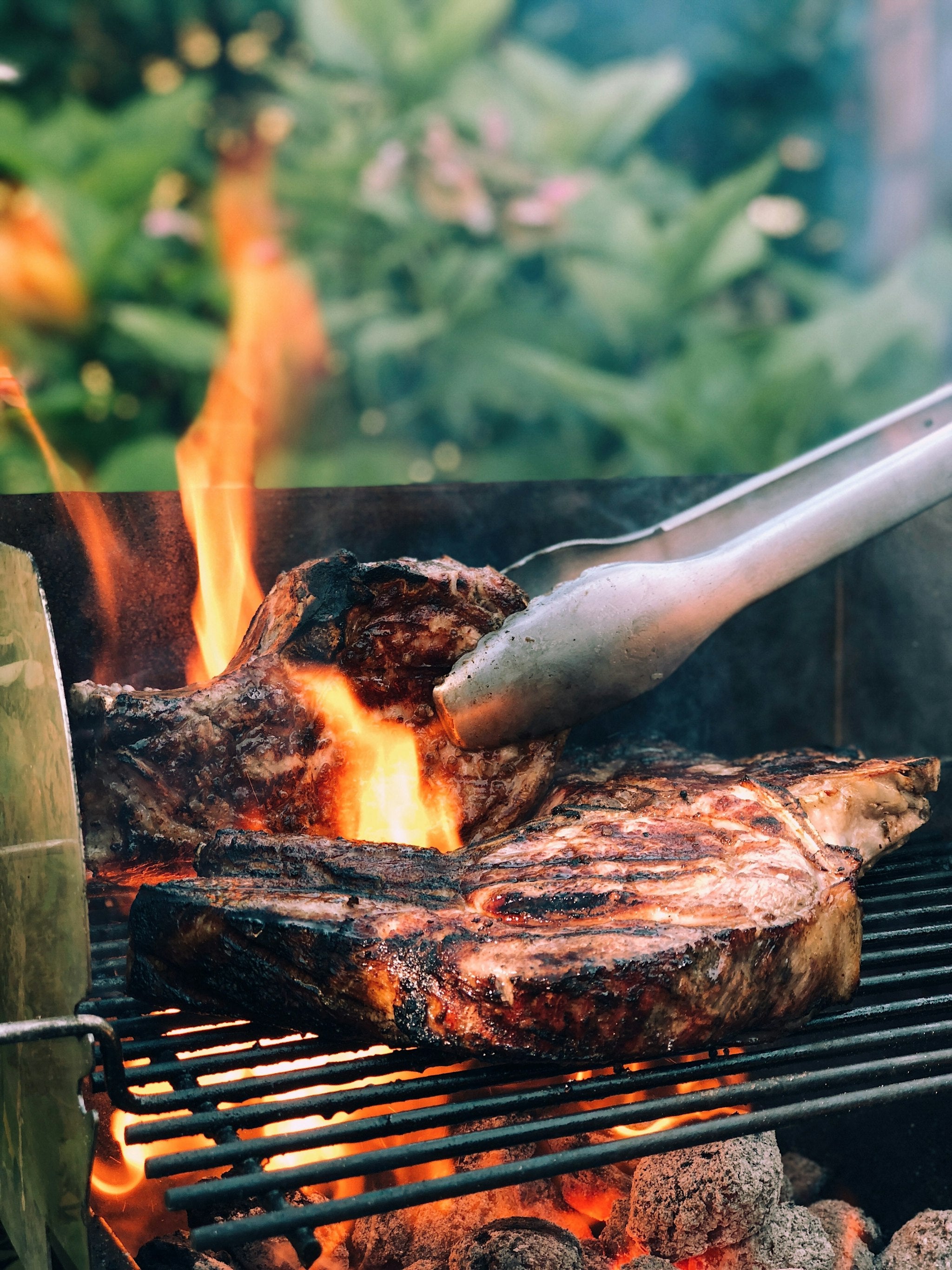 Turning thick-cut steaks with tongs over grill flames