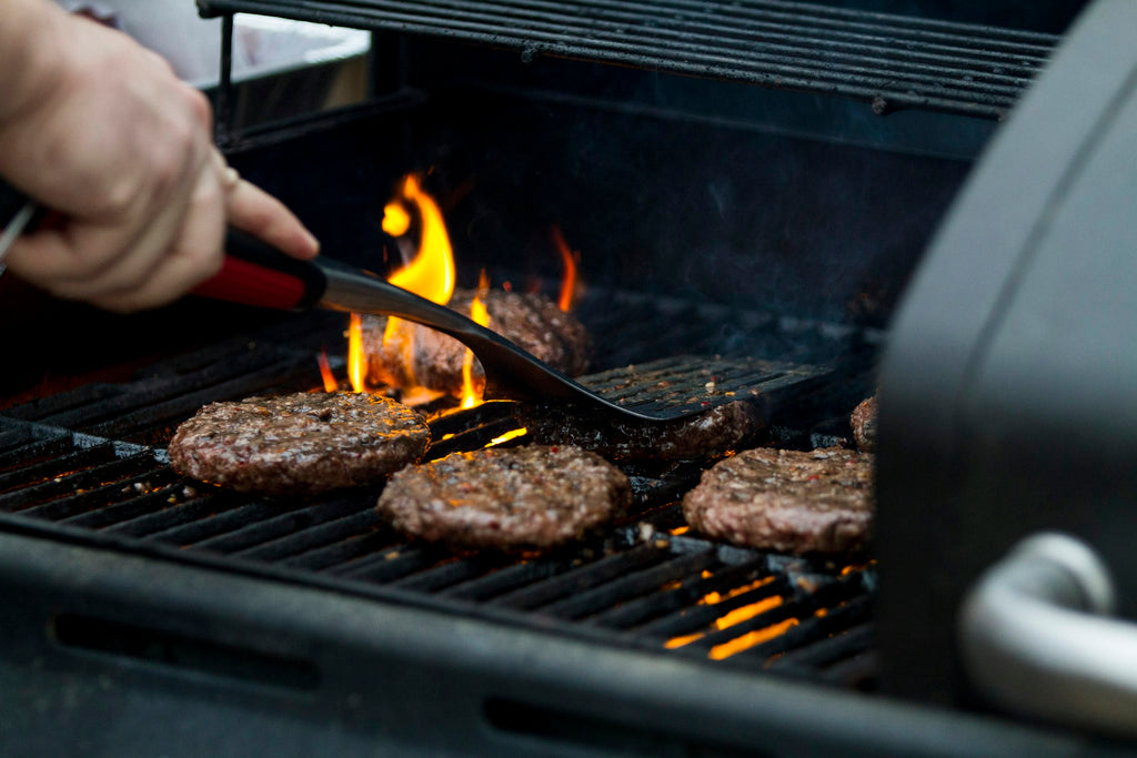Flipping burger patties over open flame on a gas grill