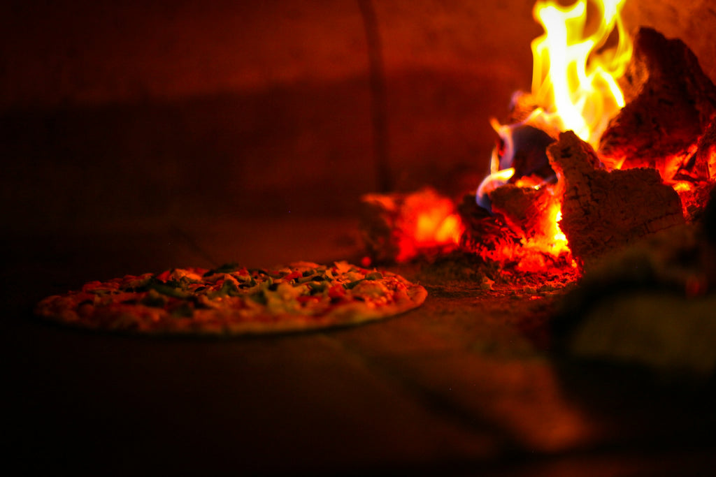 Pizza baking next to burning wood inside the oven