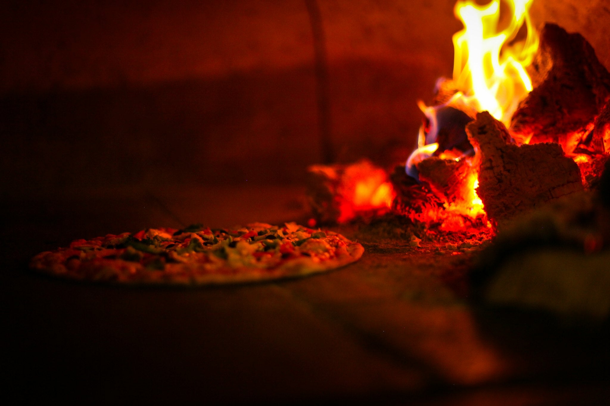 Pizza baking next to burning wood inside the oven