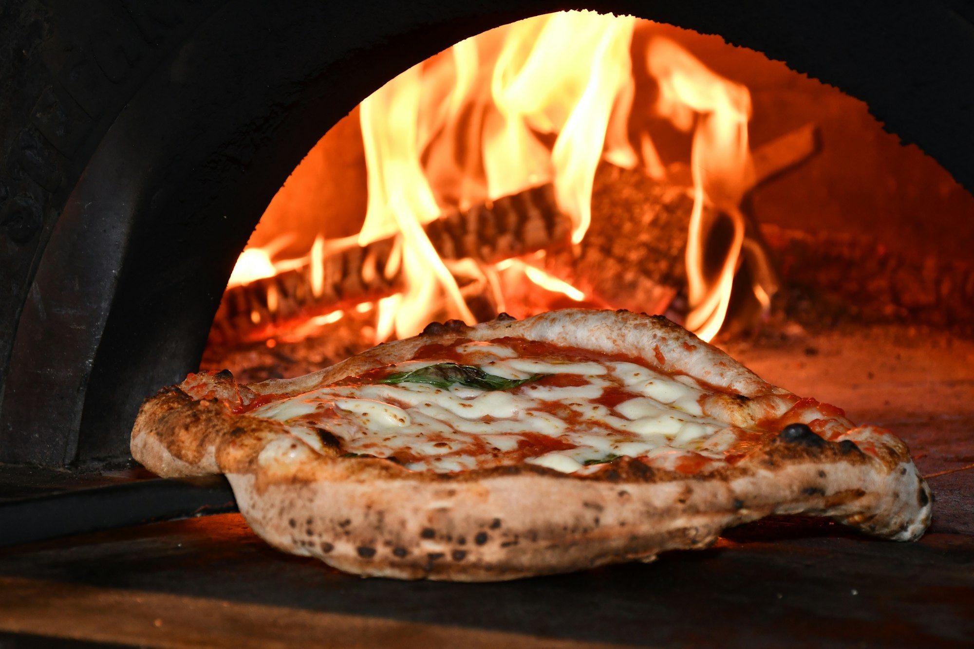 Wood-fired pizza oven with flames baking a Neapolitan pizza