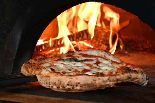 Wood-fired pizza oven with flames baking a Neapolitan pizza